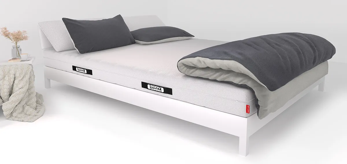 Op een bed liggen twee kussens en een groot dekbed.